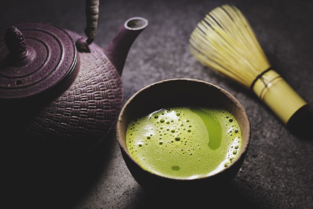 Green matcha tea powder in cups with traditional iron kettle.